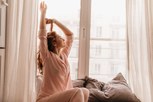  Woman stretching by the window in the morning, sitting on bed.